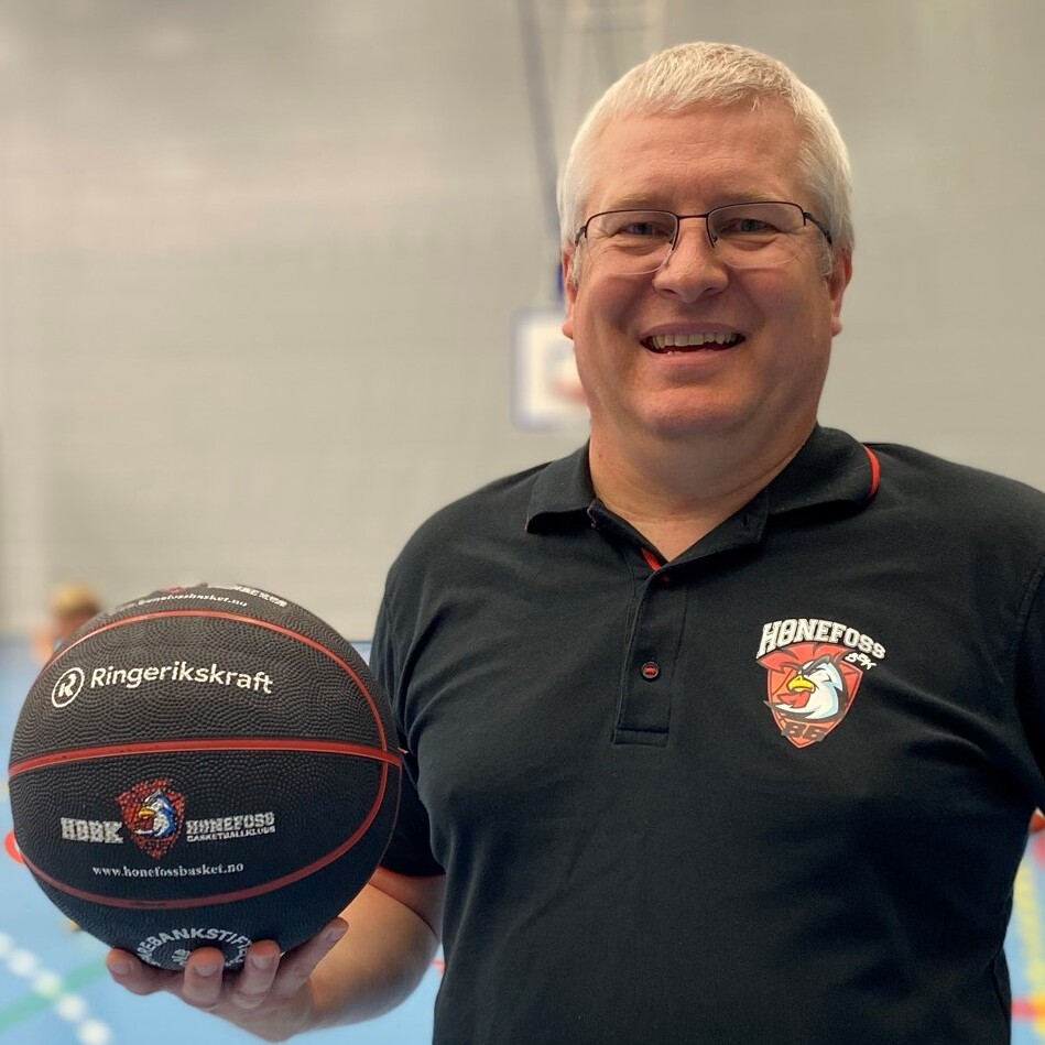 En smilende Tomas Johansen fra Hønefoss Basketballklubb står i innendørs hall og holder opp en basketball 